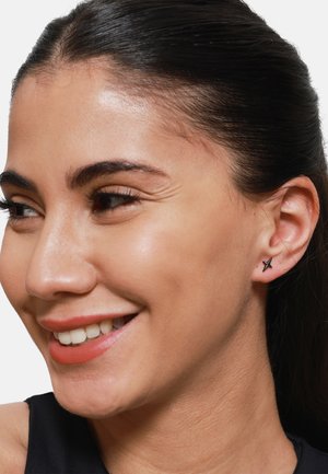Orecchini a stella nera a forma di chiodo esposti su una persona dalla pelle liscia, che mostrano il design minimalista degli orecchini e la loro finitura lucida e discreta.