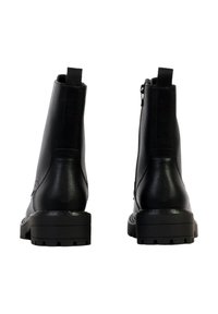 Paire de bottines en cuir noir avec semelles épaisses, languettes arrière pour tirer et fermetures éclair latérales, vue de dos sur un fond blanc.