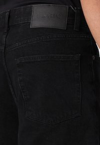 Sorte denimjeans med en glat tekstur, der har en højre baglomme og en rektangulær læderlap mærket "ONLY & SONS."