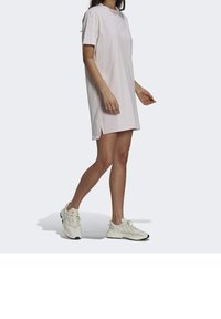 Różowa sukienka z krótkim rękawem i bocznymi rozcięciami, wykonana z miękkiego materiału. Połączona z białymi butami sportowymi z czarnymi akcentami.