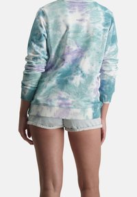 Sudadera en tonos azul claro y blanco con efecto tie-dye y detalles en morado, con un cuello redondo y puños acanalados, combinada con pantalones cortos de mezclilla.