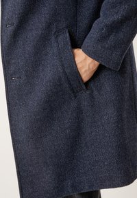 Cappotto in misto lana blu navy con tessuto testurizzato, una tasca laterale e dettagli di cucitura sottili. Il design presenta una silhouette dritta.