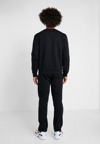 Sudadera negra y pantalones de chándal, corte relajado. Tela suave con mangas y cintura elásticas. Las zapatillas tienen acentos en blanco, rojo y azul.