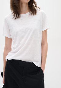 Tricou alb cu maneci scurte, realizat dintr-un material ușor, asortat cu pantaloni negri cu talie înaltă. Tricoul are o croială lejeră și o textură subtilă.