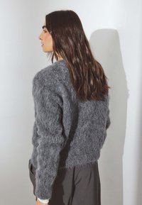 Suéter gris difuso con un acabado texturizado y esponjoso, con mangas largas, combinado con pantalones oscuros y holgados. Vista de perfil lateral.