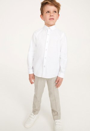 Camicia bianca con colletto, abbinata a pantaloni grigi chiari e sneakers bianche. La camicia presenta un piccolo logo sul petto.