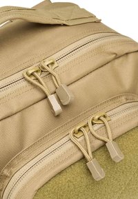 Sac à dos en tissu tan avec deux compartiments zippés dotés de tirettes de fermeture éclaire beiges et de bretelles renforcées. Surface texturée avec une couture durable.