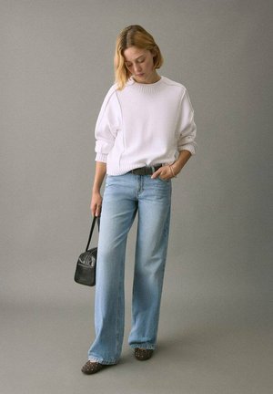 Bílý pletený svetr, světle modré džíny s širokými nohavicemi, černá kabelka, hnědé boty s cvočky. Jednoduchý design a neutrální barvy.