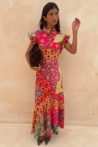 Kleurijke, gemusterde maxi-jurk met ruches aan de mouwen, een hoge kraag en een mix van gedurfde prints in rood, roze, oranje en geel. Bruine handtas.