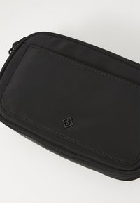 Pochette en tissu noir avec une surface texturée, dotée d'une fermeture éclair lisse et d'un petit logo en relief sur le devant.
