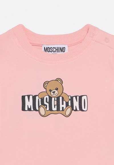 Camiseta rosa para bebé con cuello acanalado, botones de presión en el hombro y gráfico de un osito sosteniendo el texto "Moschino".