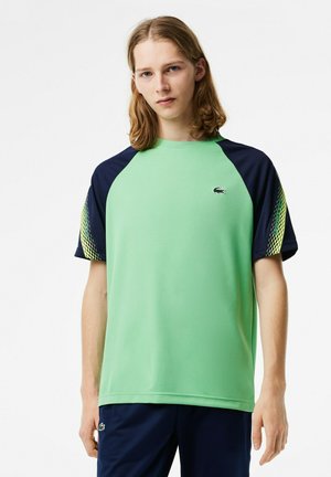 T-shirt vert à manches courtes avec des manches raglan bleu marine, présentant un motif texturé sur l'épaule et un petit logo sur la poitrine.