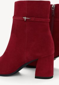 Bottines en suède rouge avec un talon carré, dotées d'une fermeture éclair latérale, d'une sangle décorative et d'une texture lisse.