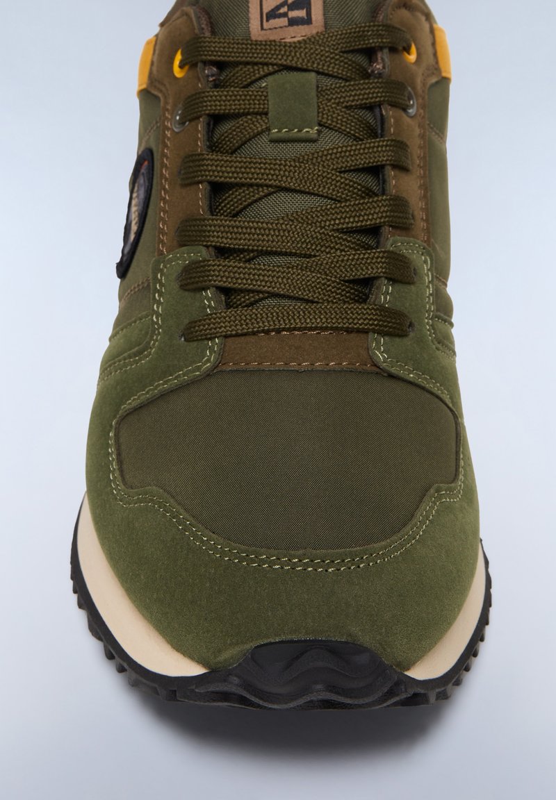 Zapatilla deportiva verde que combina ante liso y texturizado con materiales de nylon, con cordones y una suela de goma negra. Detalles de acento amarillos.