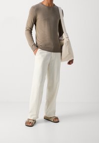 Brązowy sweter z długim rękawem, off-white lniane spodnie, beżowe sandały z klamrą oraz lekka torba płócienna na ramię.