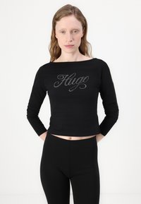 Svart langermet crop topp med en kontrasterende rhinestein "Hug" design. Utformet med båtutringning og tettsittende silhuett.