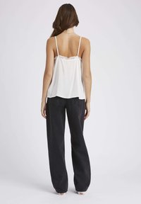 Camisole blanche avec dentelle au niveau du col, accompagnée de pantalons en denim noir amples. Le haut présente des bretelles ajustables et une coupe fluide.