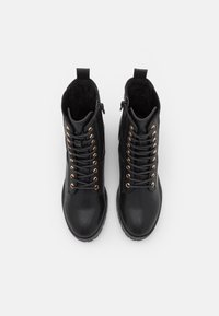 Botas de cuero negro hasta el tobillo con ojales en rosa dorado, con un diseño de cordones y cierre de cremallera, parte superior texturizada y una suela de goma resistente.