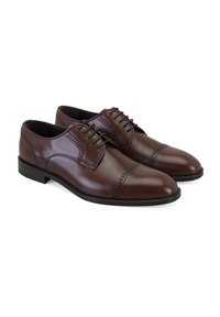 Een paar gepolijste bruine leren oxford dresschoenen met cap toe en brogue-details, weergegeven tegen een witte achtergrond.