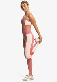 Athletic set featuring a pink and light beige crop top and leggings, with an accent of orange on the leg. The fabric is smooth and stretchy.