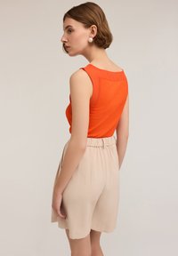 Top portocalie fără mâneci, texturată, purtat împreună cu pantaloni scurți bej până la talie. Pantalonii scurți au o talie gathered pentru un fit lejer.