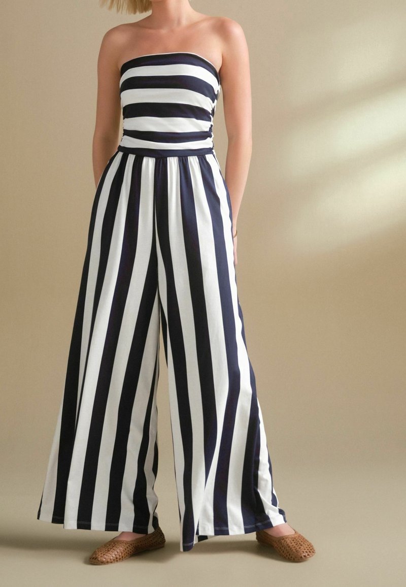 Combinaison bustier avec de larges rayures horizontales noires et blanches sur le haut et des rayures verticales sur le pantalon à jambes larges, associée à des ballerines tressées marron.