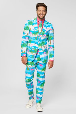 Costume bleu clair avec un motif tropical comprenant des flamants roses et des palmiers ; associé à une chemise rose et des baskets blanches.