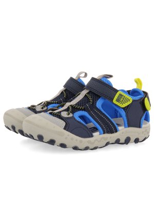 Zapatos de tiras abiertos en la parte delantera en color azul marino y azul, con parte superior de malla, detalles en gris, correas ajustables y suela de goma texturizada con patrones circulares.
