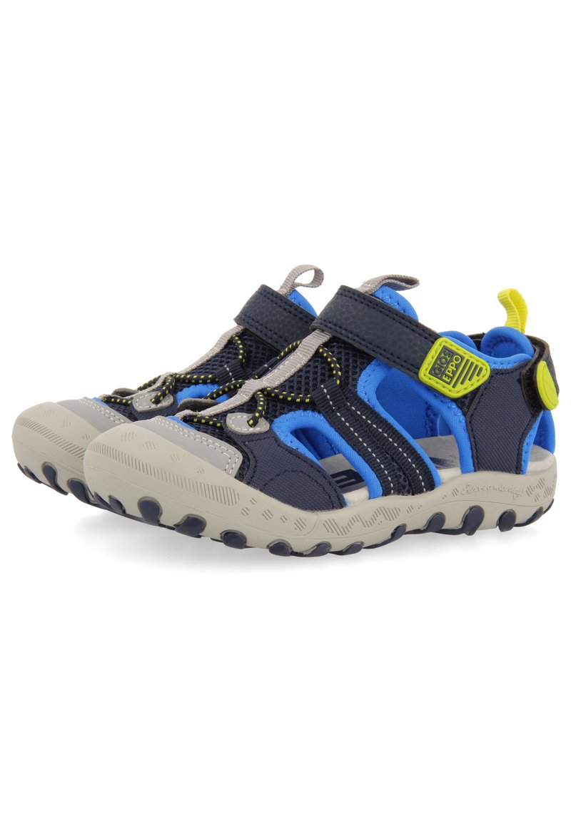 Zapatos de tiras abiertos en la parte delantera en color azul marino y azul, con parte superior de malla, detalles en gris, correas ajustables y suela de goma texturizada con patrones circulares.