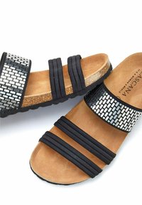 Zwarte slidesandalen met twee elastische bandjes en een gepatternde metalen bovenkant. Kurken voetbed biedt een natuurlijke textuur. Rubberen zool voor grip.