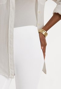 Fehér, magas derekú nadrág világos bézs, gombos inggel párosítva. Az ing enyhén texturált anyagból készült, látható gombokkal és mandzsettákkal.