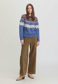 Pull en tricot bleu avec un motif Fair Isle en blanc, rose et orange ; assorti à un pantalon large en velours côtelé marron et des talons beiges.