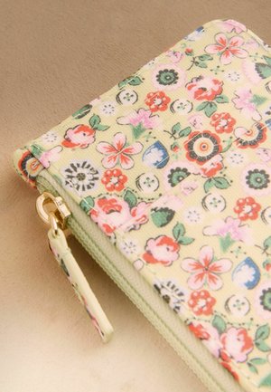 Sammenfoldet lysegrøn pung med lynlås, dekoreret med et farverigt blomster- og knapmønster på en beige overflade.