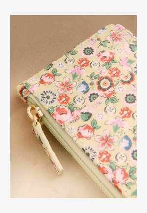 Sammenfoldet lysegrøn pung med lynlås, dekoreret med et farverigt blomster- og knapmønster på en beige overflade.