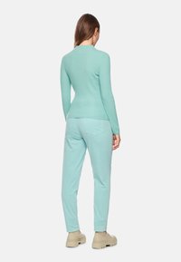 Hellblau gestreifter Langarmoberteil, kombiniert mit passenden mintfarbenen Hosen. Das Outfit zeichnet sich durch eine taillierte Silhouette und weichen Stoff aus.