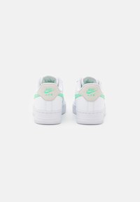 Valkoiset Nike Air -lenkkarit mintunvihrein yksityiskohdin, joissa on sileä nahkapintainen viimeistely, pyöristetty muoto ja pehmustettu kaulus mukavuutta varten.