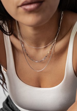 Silberne geschichtete Halsketten mit Box- und Glieddesigns, die vor nackter Haut präsentiert werden. Die oberste Kette ist eine zarte Kette.