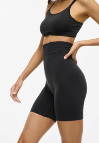 Pantaloni corti sportivi neri realizzati in materiale elasticizzato con una vita alta, texture liscia e lunghezza fino a metà coscia, caratterizzati da cuciture minime.