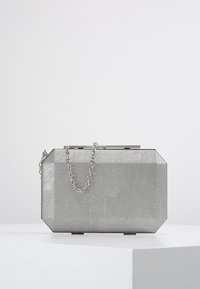 Rectangular silver clutch purse with textured surface and thin chain strap resting on a white pedestal against a light background.