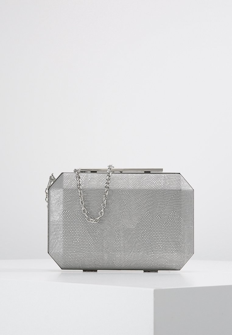 Rectangular silver clutch purse with textured surface and thin chain strap resting on a white pedestal against a light background.