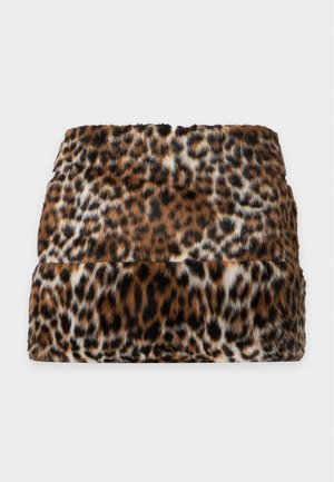 Femme portant une veste en fausse fourrure imprimé léopard et une jupe assortie, un top noir et des sandales noires à talons hauts, debout sur un fond blanc.