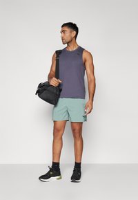Tenue de sport comprenant un haut sans manches violet foncé, un short vert menthe et des baskets noires, avec un sac de sport noir porté sur une épaule.