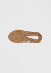 Baskets blanches avec une semelle extérieure en caoutchouc texturée de couleur tan. Elles présentent une tige lisse, un matériau flexible et une semelle à motifs pour une meilleure adhérence.