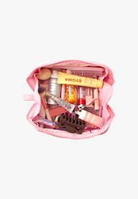 Roze cosmeticazak gevuld met verschillende schoonheidsproducten, waaronder tubes, flessen, een make-up spons, kwasten en een haarspeld.