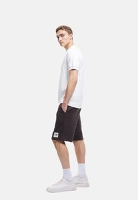Witte t-shirt met korte mouwen, gecombineerd met donkergrijze shorts met een zijzak en logo-embleem, compleet met witte sneakers en sokken.