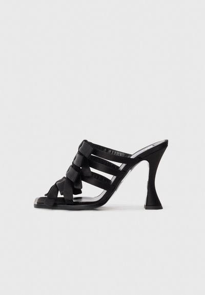 Mule en satin noir à talons hauts avec plusieurs brides et détails en nœud tressé, dotée d'un talon évasé et d'un bout carré sur fond blanc.