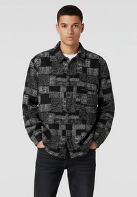 Zwart en grijs geruit shirt met een button-down ontwerp, textuurstof en een borstzak, gecombineerd met donkere jeans.