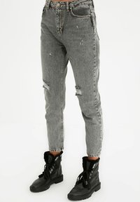 Jean gris usé taille haute, avec des genoux effilochés et une coupe droite, associés à des bottines noires à lacets.