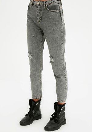 Grijze versleten jeans met een hoge taille, met gescheurde knieën en een rechte pijp, gecombineerd met zwarte veterschoenen tot de enkel.