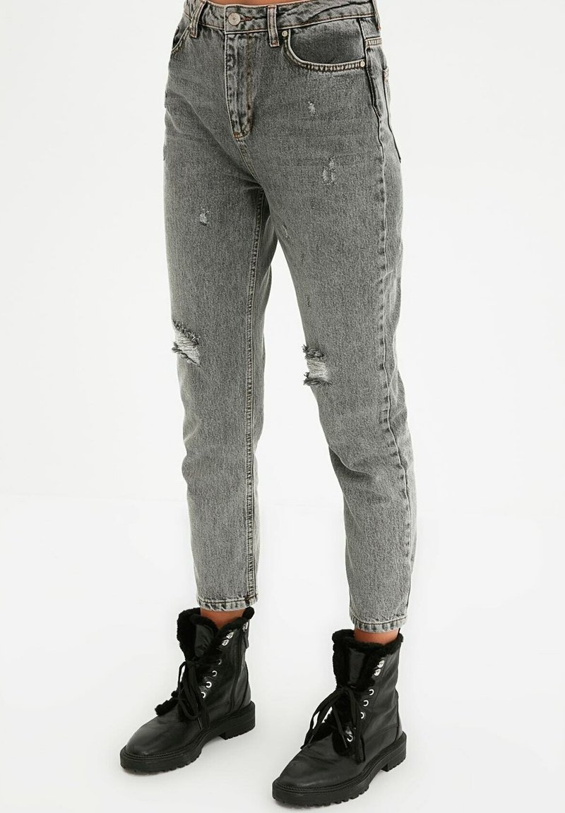 Jean gris usé taille haute, avec des genoux effilochés et une coupe droite, associés à des bottines noires à lacets.